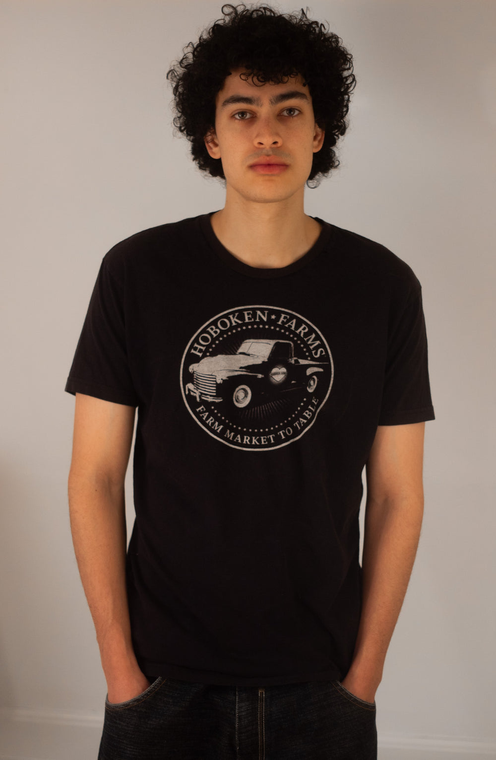 Person wearing a black t-shirt with a Hoboken Farms logo on a plain background
