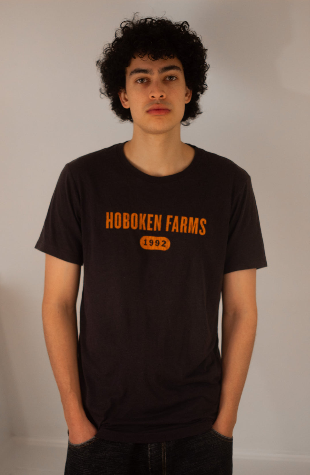 Person wearing a black t-shirt with 'Hoboken Farms 1992' text on a plain background