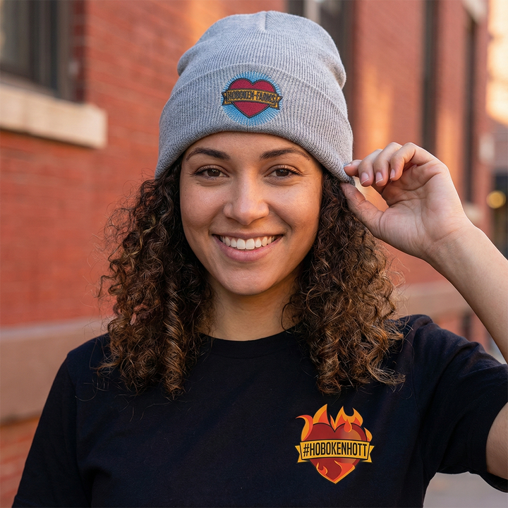 Person wearing a gray beanie with a Hoboken Farms logo and black t-shirt with a Hoboken Farms logo, standing in front of a brick building.